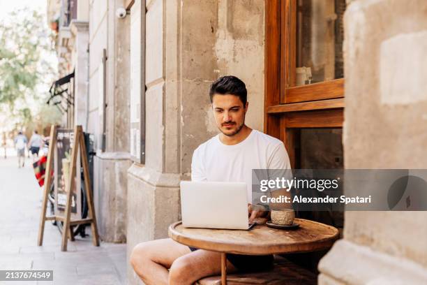 young man working on a laptop at the sidewalk cafe in summer, barcelona, spain - southern european descent stock pictures, royalty-free photos & images