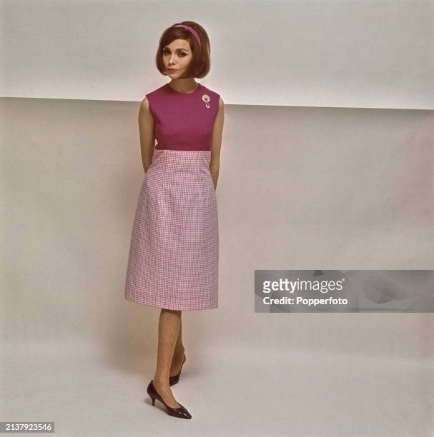 Posed studio portrait of a female fashion model wearing a sleeveless two tone pink dress featuring a pale pink gingham skirt and dark pink bodice,...