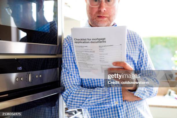 mid adult man reading mortgage application documents at home - legal documents stock pictures, royalty-free photos & images