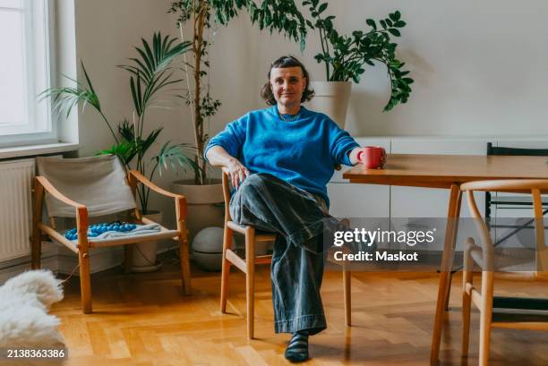 portrait of smiling mature woman sitting with coffee cup at dining table - einzelne frau über 40 stock-fotos und bilder