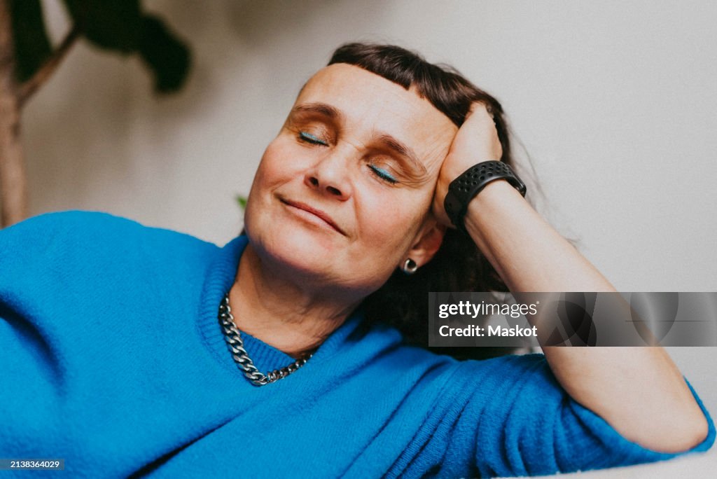 Smiling mature woman resting with head in hand at home