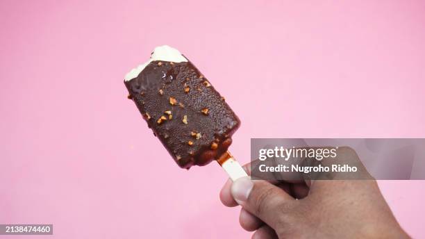almond chocolate ice cream holding by hand on pink background - eisstiel stock-fotos und bilder