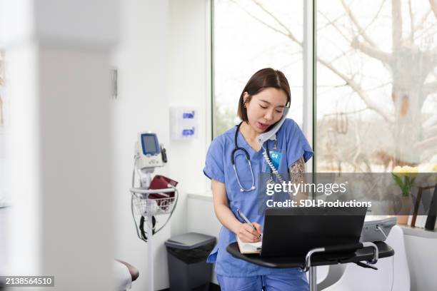 dans la salle d’examen, une interne discute avec un laboratoire sur une ligne fixe - blouse dexamen médical photos et images de collection