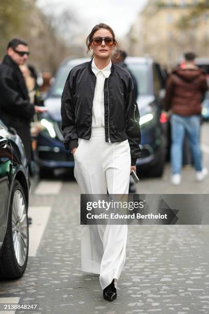 Olivia Palermo wears sunglasses, white shirt, a black bomber jacket, white oversized palazzo pants, black pointed shoes, outside Nina Ricci, during...