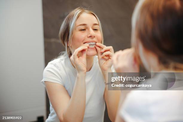 donna che toglie il suo fermo chiaro nello specchio del bagno - sbiancamento dentale foto e immagini stock