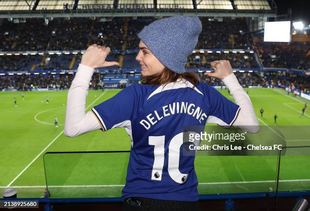 Actress Cara Delevingne poses for a photograph whilst wearing a Chelsea shirt which reads "Delevingne 10" during the Premier League match between...