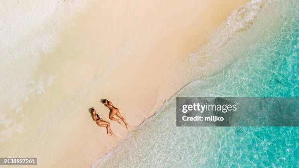two beautiful young women relaxing and sunbathing on beach. aerial view - sunbathing stock pictures, royalty-free photos & images