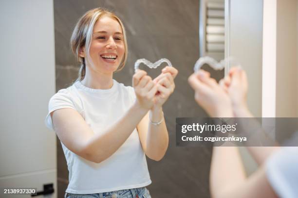 woman taking off her clear retainer in the bathroom mirror - aparelho dentário imagens e fotografias de stock