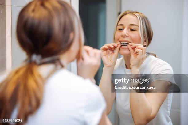 donna che toglie il suo fermo chiaro nello specchio del bagno - apparecchio ortodontico foto e immagini stock
