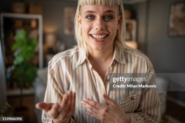 portrait of a young woman standing in the living room shooting a video for her vlog, looking at the camera and talking to her followers on social media - webcam stock-fotos und bilder