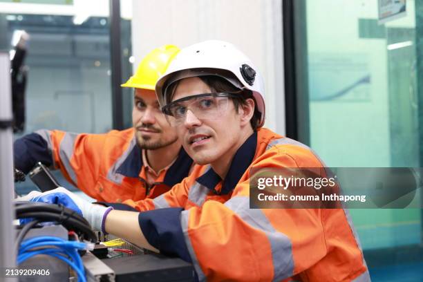 two skilled mechatronics engineers, equipped with safety ppe, are diligently conducting maintenance and configuring an advanced automation system at the factory. - configuring stock pictures, royalty-free photos & images