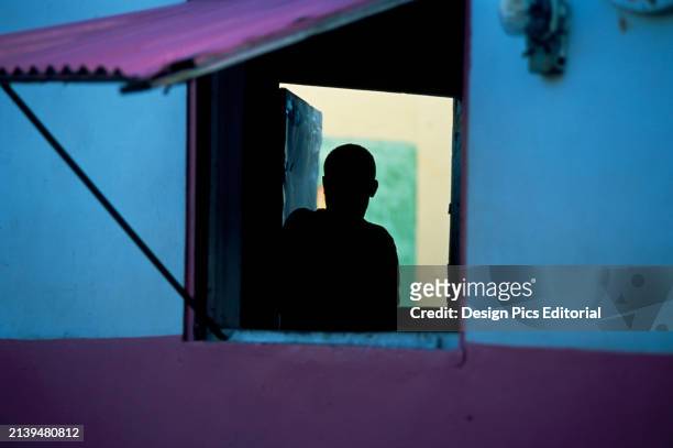 Silhouette of a boy looking through an open window of a colorful building. Commonwealth of Dominica.