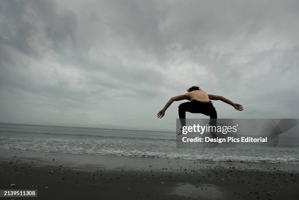 Woman Jumping On Beach Under Cloudy Skies