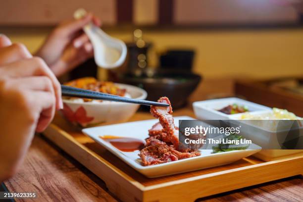 in einer nahaufnahme ist zu sehen, wie ein junger erwachsener ein bento nach taiwanesischer art genießt, eine verpackte mahlzeit, die aus geschmortem schweinereis, suppe und beilagen besteht. - schweinebauch stock-fotos und bilder