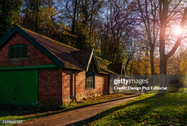 Friends walk on a trail past a brick building in a park in Durham at sunset. Durham, Durham, England.