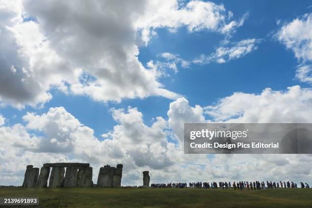 People Standing In A Row Looking Around Stonehenge. Wiltshire, England.