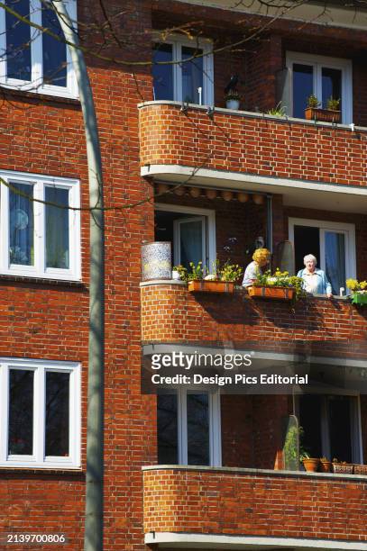 Friends Enjoying The Balcony In A Brick Building. Hamburg, Germany.