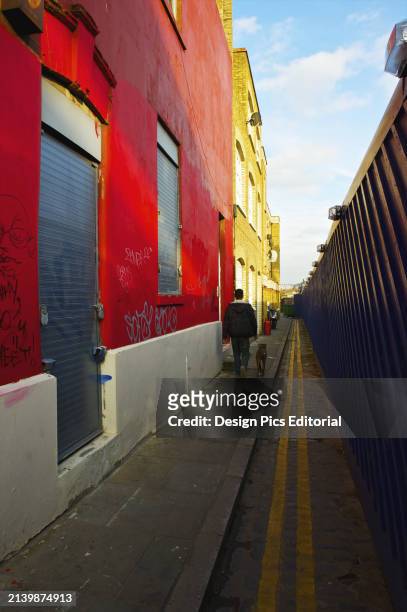 Pedestrian and Dog Walking Down A Narrow Alley Beside Colourful Buildings. London, England.