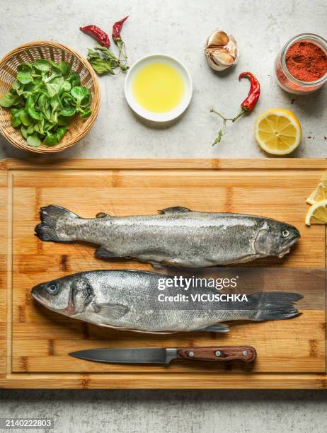 raw whole trout fishes on wooden cutting board and ingredients for healthy cooking - trout stock pictures, royalty-free photos & images