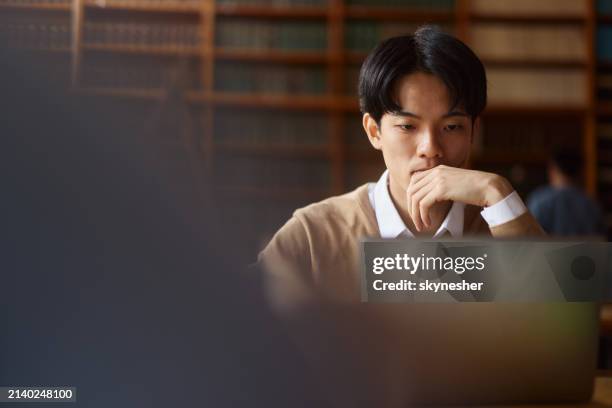 estudiante universitario asiático usando una computadora portátil mientras estudia en la biblioteca. - biblioteca fotografías e imágenes de stock