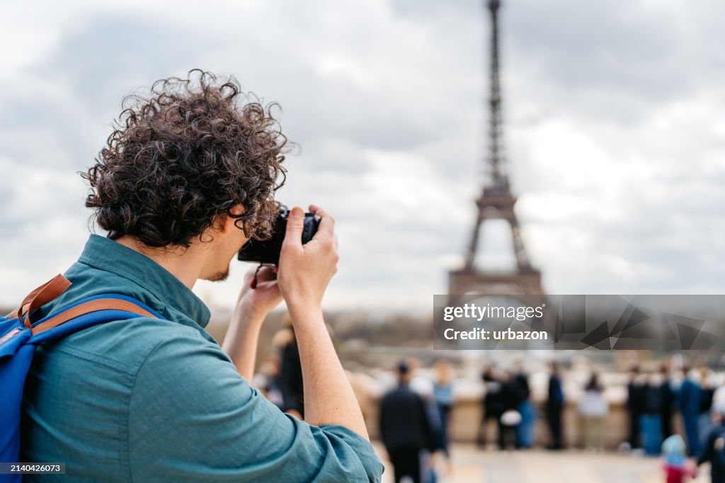Young Male Tourist Taking Pictures Using A Camera Of An Eiffel Tower In Paris In France