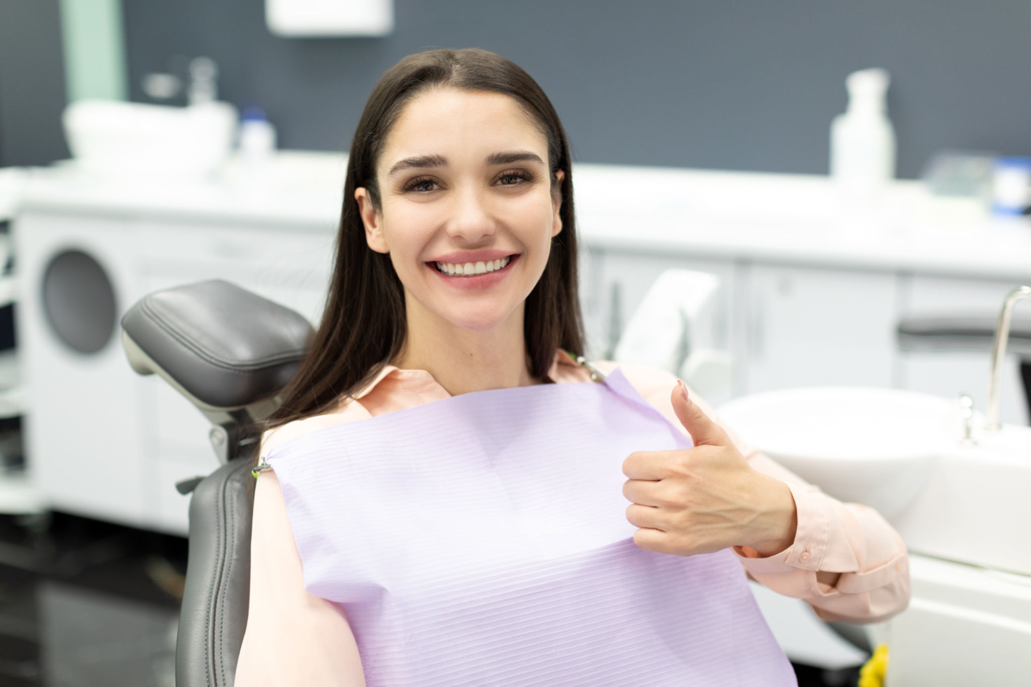 Hermosa paciente femenina feliz que muestra el pulgar hacia arriba después del tratamiento dental, sentada en la silla en la clínica estomatológica moderna después del chequeo Hermosa paciente femenina feliz que muestra el pulgar hacia arriba después del tratamiento dental, sentada en la silla en la clínica estomatológica moderna después del chequeo