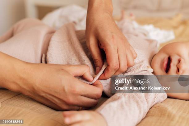 mother with her infant baby daughter during changing the clothes on bed at home. - changing diaper stock pictures, royalty-free photos & images