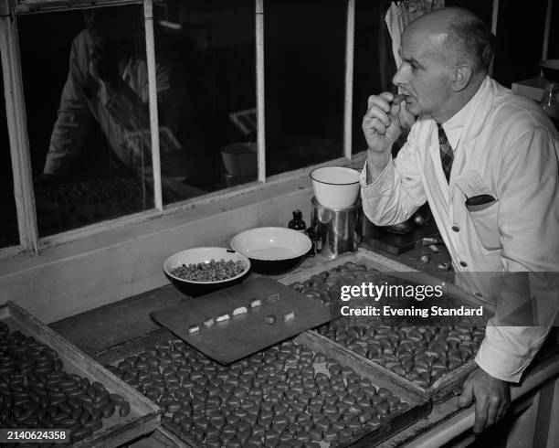 Man wearing a white lab coat tastes chocolates laid out on a tray in front of him at the Nestlé factory in Hayes, Middlesex, November 25th 1953.