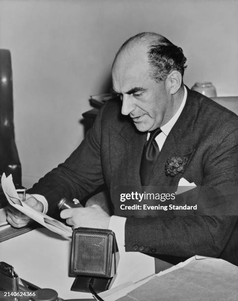 British comedian and radio presenter Kenneth Home seated at a desk and holding a microphone, December 2nd 1953.