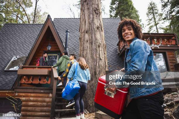 low angle view of smiling man carrying red cooler with friends in background - casita de campo fotografías e imágenes de stock