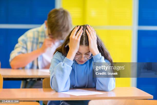 trauriges teenager-mädchen sitzt im klassenzimmer - schulische prüfung stock-fotos und bilder