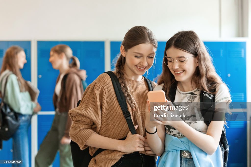 Adolescentes usando o telefone inteligente no corredor da escola