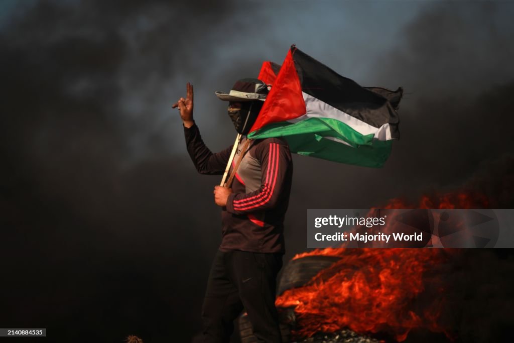 Palestinian youth hold flags next to burning tyres during a protest