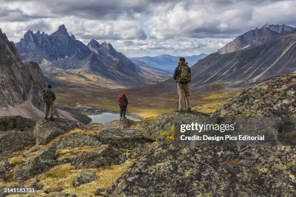 Group of Hikers Standing on Rocks Overlooking The Colourful Valleys In Tombstone Territorial Park In Autumn. Yukon, Canada.