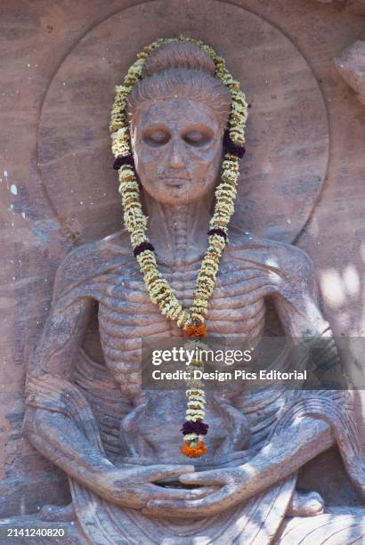 India, Bihar, Statue of the Buddha at the Mahabodhi Temple depicting his austerity/starvation phase. Puja flowers around his body. Bohdgaya.