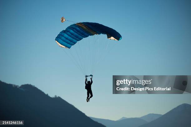 Skydiver Floats With A Parachute Against A Blue Sky and The Swiss Alps. Locarno, Ticino, Switzerland.