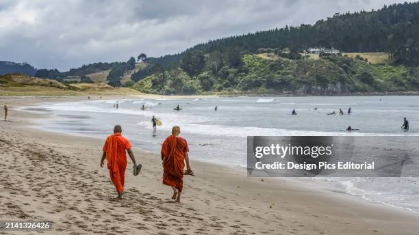 Buddhist Monks walking on the sand of Hot Water Beach. An underground river of hot water flows from the interior of the earth to surface in the...