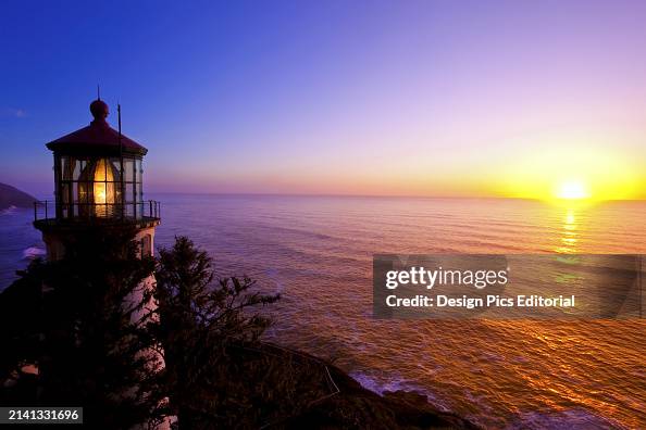 Heceta Head Light at sunrise with the bright sun rising above the tranquil pacific ocean and casting colourful reflections on the water, Pacific Northwest. Oregon, United States of America