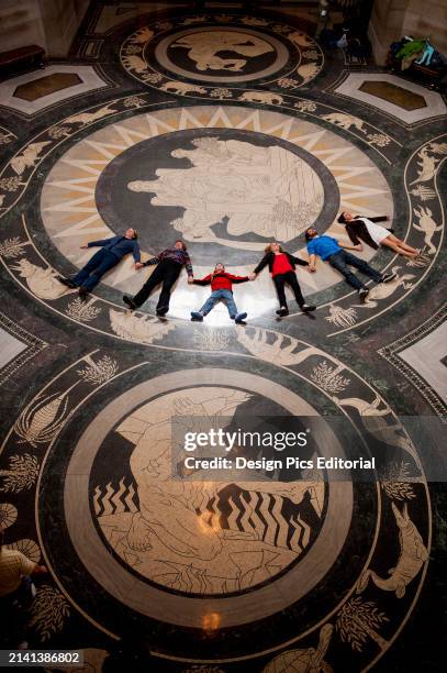 Tour group lays in a row on the decorative Rotunda floor in the Nebraska State Capitol and looks up to admire the ceiling. Lincoln, Nebraska, United...