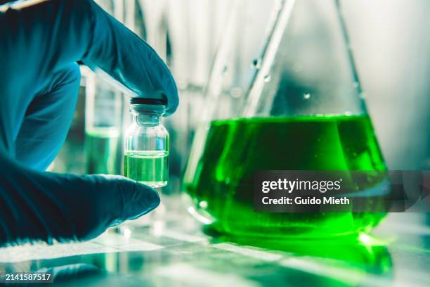 blue glove holding a green filled vial and a green filled flask. - biofuel stock pictures, royalty-free photos & images