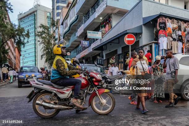 Woman stares down a motorcycle taxi driver as she crosses the street during rush hour on April 05, 2024 in Kigali, Rwanda. The motorcycle taxi is the...
