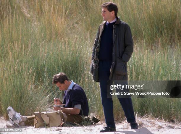 Prince Charles painting with watercolours on the beach, as his bodyguard stands nearby, during a holiday to Scotland, in August 1989.