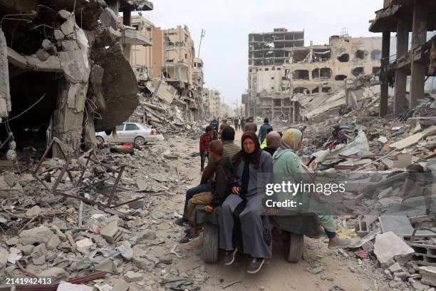 Palestinian family rides on the back of a donkey-drawn carriage next to damaged buildings in Khan Yunis on April 8, 2024 after Israel pulled its...