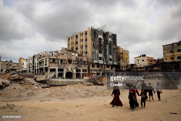 Palestinians walk past damaged buildings in Khan Yunis on April 8, 2024 after Israel pulled its ground forces out of the southern Gaza Strip, six...