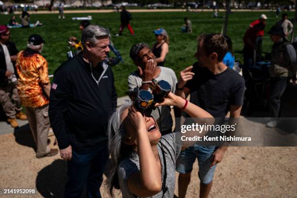 Izumi Yamamoto of Seattle, WA, looks up at the sun using binoculars outfitted with solar film, as people gather on the National Mall to view the...