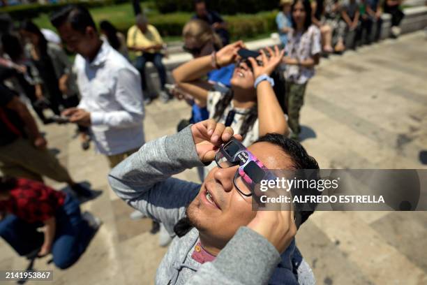 People look toward the sky as the moon begins to partially eclipse the sun outside the Fine Arts Palace in Mexico City on April 8, 2024. This year's...