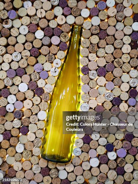 an empty and yellow bottle of wine surrounded by corks.
several corks have been patinated with red wine, others are marked by a vintage year.
studio shot in paris, france.
artificial light and natural colors. - weinkorken stock-fotos und bilder