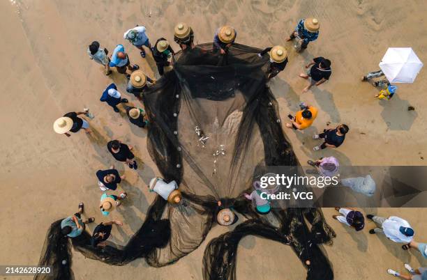 Tourists and fishermen arrange a net in preparation for fishing at Boao beach on April 6, 2024 in Qionghai, Hainan Province of China.