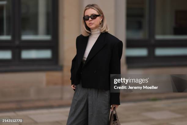 Isabelle Hartmann seen wearing Vehla Eyewear black / brown sunglasses, gold earrings, COS creamy white turtleneck top, Khaite black cropped oversized...