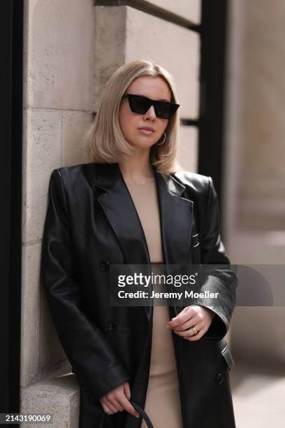 Isabelle Hartmann seen wearing Celine black sunglasses, vintage beige short dress and Magda Butrym black leather long coat on April 05, 2024 in...
